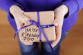 Childrens hands holding a gift or present in kraft paper and tag with note Happy Birthday, top view