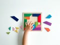 childs hand collects multicolored wooden mosaic on white background. child solves colorful tangram