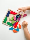 childs hand collects multicolored wooden mosaic on white background. child solves colorful tangram