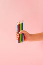 Childs hand holding crayons against pastel pink background. Back to school or happy childhood concept