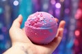 childs hand holding a glittery bath bomb over a filled bathtub