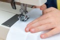 A childs hand pulling a white textil throught a sewing machine