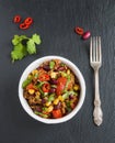 Chili con carne in a white ceramic bowl on black stone background. Cooked with ground beef, tomatoes, peppers, beans, corn, garlic