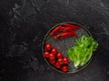 Chili peppers, cherry tomatoes, lettuce on a plate, on a black background. View from above Royalty Free Stock Photo