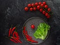 Chili peppers, cherry tomatoes, lettuce on a plate, next to cherry tomatoes and chilli peppers on a black background. View from Royalty Free Stock Photo