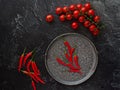 Chili peppers on a plate, next to cherry tomatoes and chilly peppers on a black background. View from above Royalty Free Stock Photo