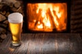 Chilled glass of light beer on the wooden table. Fireplace at the background