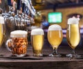 Chilled mugs and glasses of beer on the old wooden table. Pub interior and bar counter with beer taps at the background. Royalty Free Stock Photo