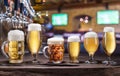 Chilled mugs and glasses of beer on the old wooden table. Pub interior and bar counter with beer taps at the background Royalty Free Stock Photo