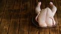 Chilled plucked chicken in a transparent plate on a rustic natural pine board