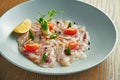 Chilled sea bass carpaccio with red onion, cherry tomatoes and hot chili peppers in a beige bowl on a wooden background. Close up Royalty Free Stock Photo