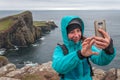 Chilled woman taking photo on a rainy day with cliffs of Neist Point behind her