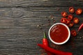 Chilli pepper and bowl sauce on wooden background, top view
