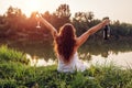 Chilling with wine. Woman enjoying glass of wine on river bank at sunset raising arms and feeling free and happy Royalty Free Stock Photo