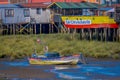 CHILOE, CHILE - SEPTEMBER, 27, 2018: Boat in low tide in front of colorful wooden restaurant cebiche on stilts palafitos
