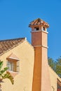 Chimney designed on roof of orange painted house building outside against blue sky background. Construction of exterior