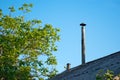 Chimney pipe over the roof of the house, against the blue sky of green trees Royalty Free Stock Photo