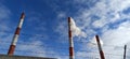 Chimneys of an industrial plant blowing smoke against a blue sky with clouds and barbed wire. Royalty Free Stock Photo