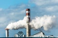 Chimneys of an industrial unit with thick, white smoke blowing out of one chimney