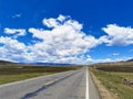 Under the blue sky and white clouds, the road leading to the distance on the grassland.