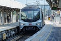 Fast metro train arrives at open-air station, people walk on platform. MTR Corporation.