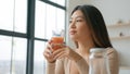 Chinese Asian woman in kitchen drinking glass fresh orange peach juice smiling girl looking away dreaming enjoy natural Royalty Free Stock Photo