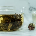 Chinese blooming tea. A glass teapot with a blooming tea flower on a white table. a cup of Chinese blooming tea and tea balls. Royalty Free Stock Photo