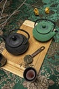Chinese cast iron teapots in black and one in green with full cups of tea, measuring spoon full of dehydrated tea Royalty Free Stock Photo
