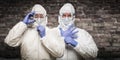 Chinese and Caucasian Men Wearing Hazmat Suit, Goggles and Mask with Brick Wall Background