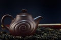 A Chinese clay teapot stands in front of a closed fan and dark background and in front of white tea from China Royalty Free Stock Photo