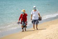 Chinese couple of elderly people walking barefoot on Sanya bay beach wearing blue surgical face masks to prevent Covid epidemic