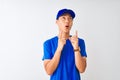 Chinese deliveryman wearing blue t-shirt and cap standing over isolated white background amazed and surprised looking up and