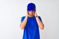 Chinese deliveryman wearing blue t-shirt and cap standing over isolated white background with hand on head for pain in head