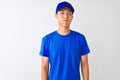 Chinese deliveryman wearing blue t-shirt and cap standing over isolated white background puffing cheeks with funny face