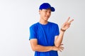 Chinese deliveryman wearing blue t-shirt and cap standing over isolated white background smiling with happy face winking at the