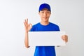 Chinese deliveryman wearing cap holding banner standing over isolated white background doing ok sign with fingers, excellent