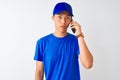 Chinese deliveryman wearing cap talking on the smartphone over isolated white background with a confident expression on smart face