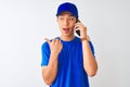 Chinese deliveryman wearing cap talking on the smartphone over isolated white background pointing and showing with thumb up to the