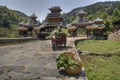 Chinese farmer carries grass on cargo scooter, near roofed bridge.