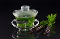 In a Chinese Gaiwan made of glass there is fresh, warm peppermint tea against a dark background with fresh peppermint and flowers Royalty Free Stock Photo