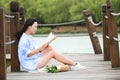 Chinese Girl reading book. Blonde beautiful young woman with book sit on bridge near fence. Royalty Free Stock Photo