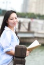 Chinese Girl reading book. Blonde beautiful young woman with book stand near fence. Royalty Free Stock Photo