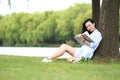 Chinese Girl reading a book under tree. Blonde beautiful young woman with book sit on the grass. Royalty Free Stock Photo