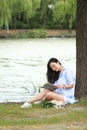 Chinese Girl reading a book under tree. Blonde beautiful young woman with book sit on the grass. Royalty Free Stock Photo