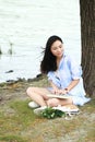 Chinese Girl reading a book under tree. Blonde beautiful young woman with book sit on the grass. Royalty Free Stock Photo