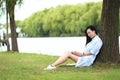 Chinese Girl reading a book under tree. Blonde beautiful young woman with book sit on the grass. Royalty Free Stock Photo