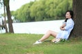 Chinese Girl reading a book under tree. Blonde beautiful young woman with book sit on the grass. Royalty Free Stock Photo