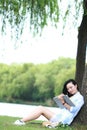 Chinese Girl reading a book under tree. Blonde beautiful young woman with book sit on the grass. Royalty Free Stock Photo