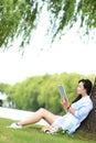 Chinese Girl reading a book under tree. Blonde beautiful young woman with book sit on the grass. Royalty Free Stock Photo