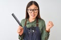 Chinese hairdresser woman wearing glasses holding comb over isolated white background screaming proud and celebrating victory and Royalty Free Stock Photo